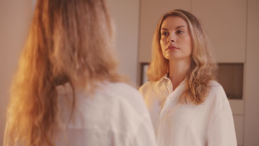 Beauty morning routine happy woman combing her blonde hair, smiling face eyes looking at mirror reflection comb gets tangled curls. Girl strands brushing, combs dry porous wavy long bleached hair care
