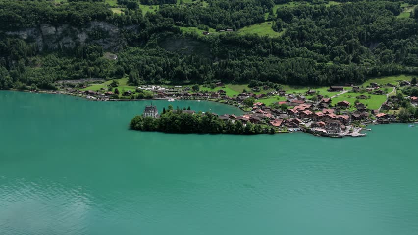 Aerial of the beutiful small village of Iseltwald at the turquoise lake Brienzersee surrounded by the alp mountainens showing Castle seeburg and revealing da distant view near Interlaken Switzerland