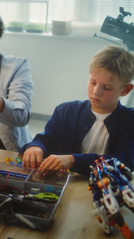 Team of Kids and Young Teacher Assembling Constructor on STEM Lesson in Multiethnic Classroom. Primary School Children Exploring Robotics, Renewable Energy Models, Studying Technologies. Vertical Shot