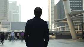 Businessman walks across urban square at modern downtown block backside view. Company CEO young man strolls observing stylish architectural forms of megapolis. Business success - Powered by Shutterstock - Get 15% off with code: PIKWIZARD15