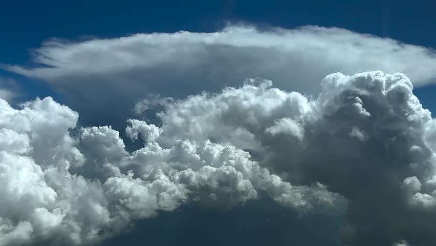 an aerial view taken from a jet cockpit flying at cruise through a sky full of storm clouds, and a anvil shape cumulonimbus ahead, under a blue sky. Ultra-realistic 4K.