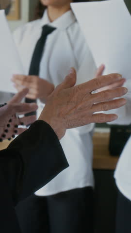 Vertical of unrecognizable nun holding rosary beads directing choir of diverse student girls in white uniforms singing in modern Christian school