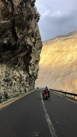 Scenic Skardu road near Chilas with rugged mountains, deep gorge with flowing river, and a daring biker riding towards adventure on winding highway. Stunning landscape perfect for travel footage.