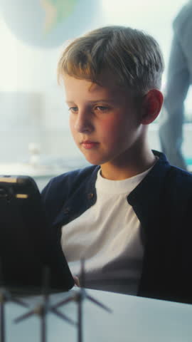 Elementary School Boy Writing Code for Advanced Automated 3D Printer on Tablet Computer During Programming Lesson. Smart Young Boy Studying Technology in Classroom. STEM Education. Vertical Shot.