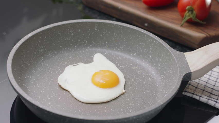   Process of breaking an egg on a frying pan for cooking sunny side up fried egg.