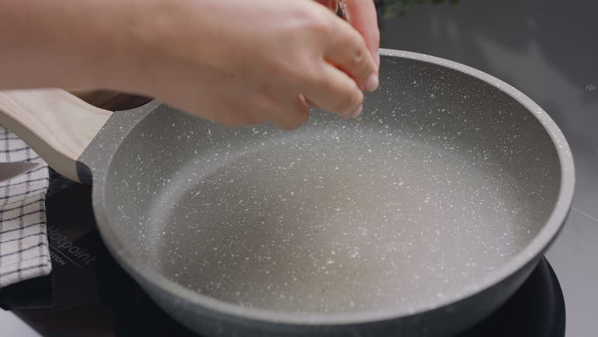   Process of breaking an egg on a frying pan for cooking sunny side up fried egg.