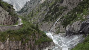 Aerial video of narrow mountain gorge with a river, cascading waterfall, rugged cliffs, and winding road, capturing dynamic alpine scenery and flowing turquoise water. - Powered by Shutterstock - Get 15% off with code: PIKWIZARD15