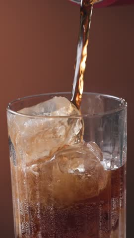 Closeup of pouring cola drink with ice cubes. Fizzing cola with ice in glass. Refreshing tasty cola drink.