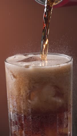 Closeup of pouring cola drink with ice cubes. Fizzing cola with ice in glass. Refreshing tasty cola drink.