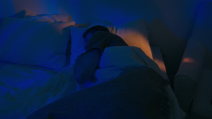 Caucasian man turning over in bed while sleeping peacefully in bedroom illumed moonlight