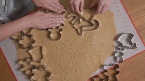 A mother's and a child's hands work in unison pressing metal cookie cutters into raw gingerbread dough. They collaborate to create a festive pattern of holiday shapes for Christmas baking. - Powered by Shutterstock - Get 15% off with code: PIKWIZARD15