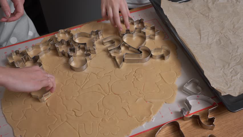 Hands carefully separate the leftover dough from the freshly cut cookie shapes. The metal cutters are lifted away one by one, revealing the final forms ready for the baking sheet.