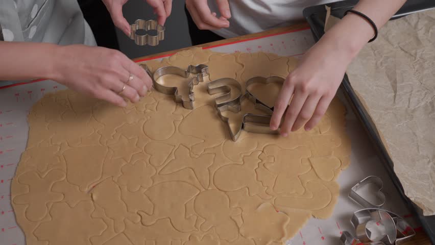 Hands carefully lift and remove metal cookie cutters one by one from the rolled-out dough. This reveals a pattern of perfectly cut, raw gingerbread cookie shapes ready to be baked.