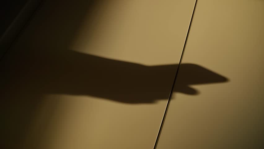 Shadow of male hands holding mobile phone typing and sending text messages. Businessman person sending sms or using and working with smartphone. Silhouette on wall during sunset or sunrise light