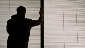 Man leaning on window with shutters or venetian blinds talking on the phone. Young businessman or student holding mobile phone speaking in office or apartment home. Business deal or important call - Powered by Shutterstock - Get 15% off with code: PIKWIZARD15