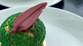 Gourmet choux pastry dessert with vibrant green craquelin topping and a decorative chocolate garnish, presented on a white plate, slow motion - Powered by Shutterstock - Get 15% off with code: PIKWIZARD15