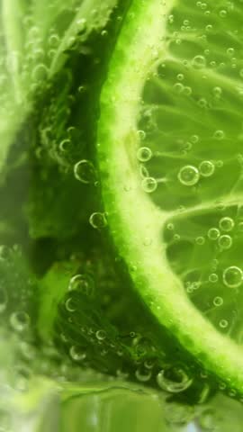 Macro shot of mojito cocktail with fresh slices lime mint and ice rotate in circle. Bubbles in glass with carbonated drink. Summer drink. Vertical shot