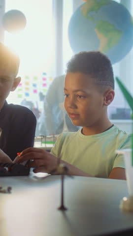 Team of Multiethnic Talented Boys Sitting at Table, Studying Robotic Arm Model. Primary School Children During Science Lesson in Modern Classroom. Interactive Learning, STEM Education. Vertical Shot.