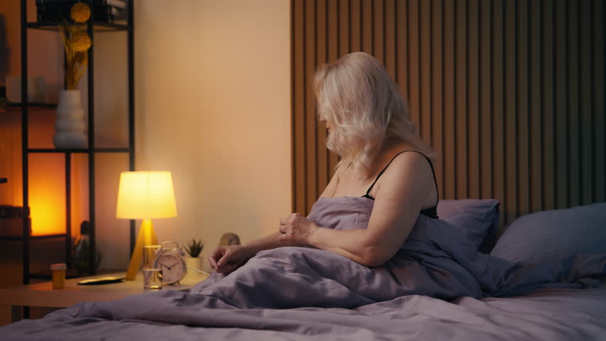 Mature woman taking supplement with water before sleep, personal healthcare