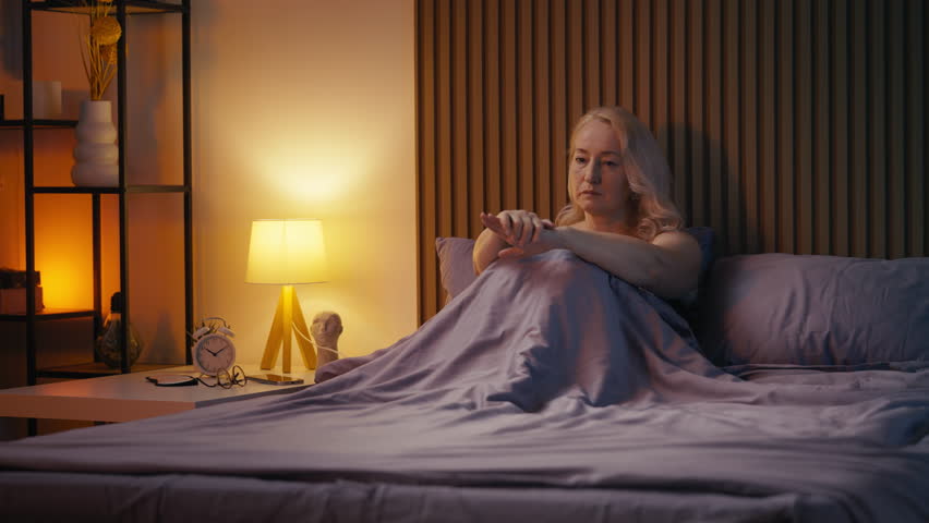 Mature woman feeling depressed while sitting in bed, struggling with life crisis