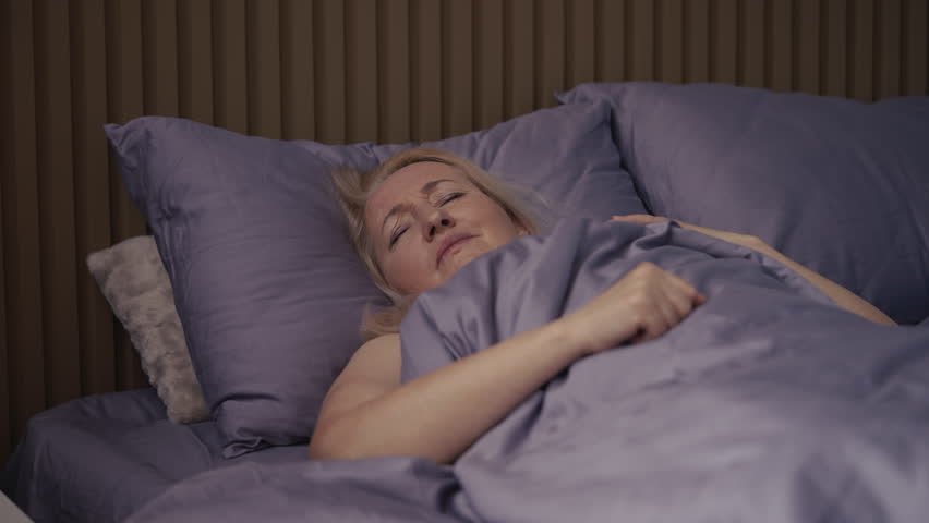 Middle-aged woman suffering from headache while lying in bed, health discomfort