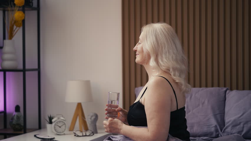 Attractive middle-aged woman taking vitamins with water, morning wellness ritual