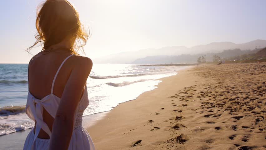 Attractive woman walking on the beach at sunset. Slow Motion.