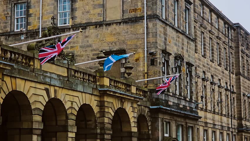 Scottish and British flags hanging on historic stone building in Edinburgh. National symbols fluttering on facade of old architecture in Scottish capital. Flags waving on government structure in
