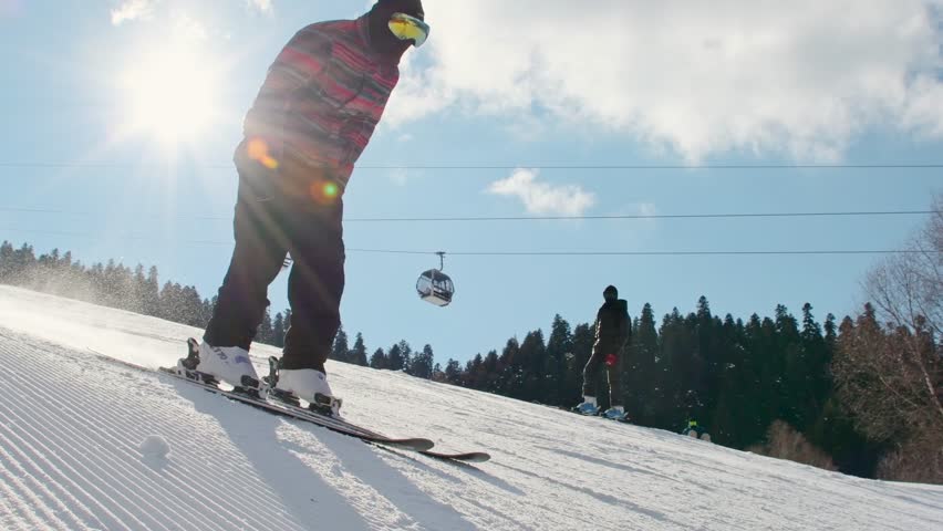 Young male beginner skiers friends enjoy skiing on groomed snow slope under bright winter sun during ski vacation learning to ski in ski resort. Intentional out of focus background copy space