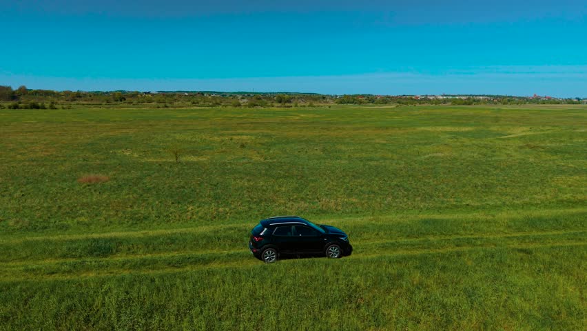 Driving SUV across grassy off-road track through open meadow. Moving car along uneven terrain surrounded by green fields. Cruising vehicle through wide countryside landscape