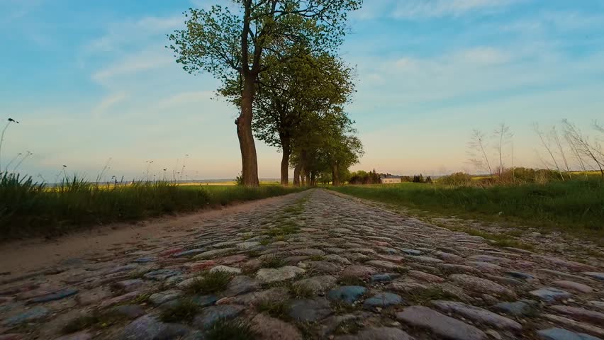 POV car driving by Poland rural road at sunset. Sunset POV ride along cobblestone country path in Polish village. Rural evening view of car moving over stone road through countryside