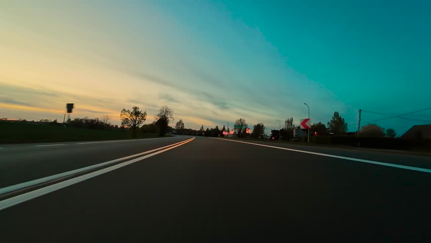 POV driving car on curving asphalt road at sunset while truck passing with headlights on. Point of view moving vehicle along bending paved route during dusk as lorry speeding with lights shining