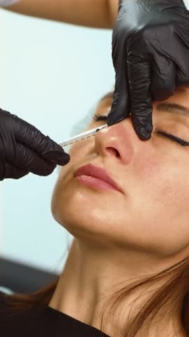 Beautician injecting dermal filler into nose bridge area for non-surgical correction, vertical orientation. Aesthetic practitioner performing liquid rhinoplasty with hyaluronic acid. Cosmetic