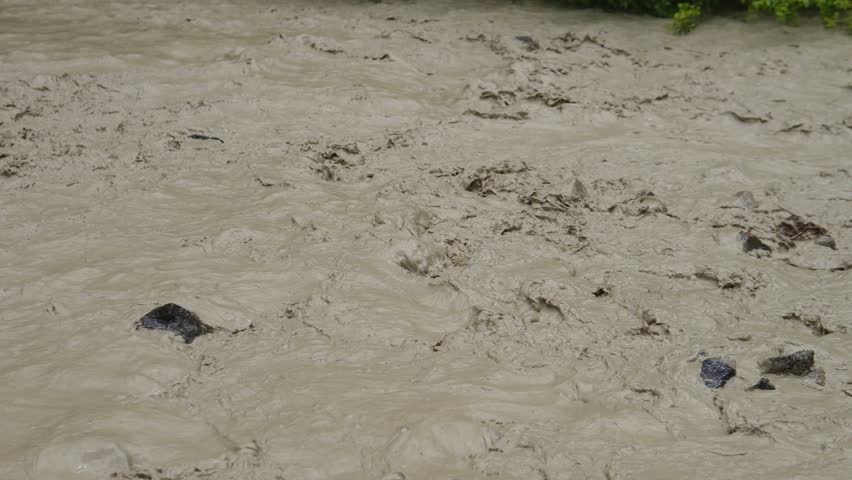 Brown river flows after rain. After heavy rains in the mountains, the mountain river turned into a muddy, fast flow. Heavy rains caused a sudden rise of water, carrying away soil.