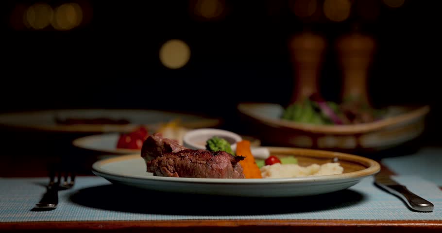 Gourmet steak dinner plate with vegetables in elegant restaurant setting. Luxurious fine dining experience focused on culinary artistry and sophistication.