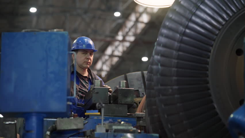 A Worker is inspecting the turbine generator produced at the manufacturing plant. A Worker is examining the parts of the turbine generator. A Worker is testing the quality of the turbine generator.
