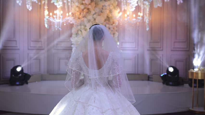 The back of a young bride in a white lace wedding dress, who goes to the groom during the ceremony