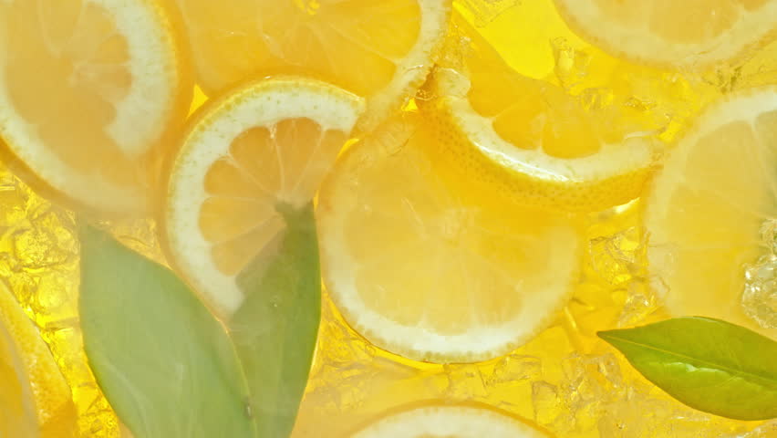 Super Slow Motion Shot of Pouring Lemonade on Fresh Lemon Slices, Ice and Green Leaves at 1000fps.