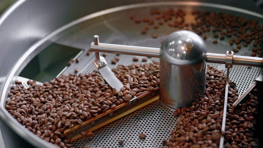Process roasting brown coffee beans on professional mixing roaster industry machines.