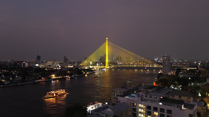 Aerial view of illuminated Rama VIII Bridge at night. Cable-stayed bridge crossing Chao Phraya River in Bangkok, Thailand, 4k