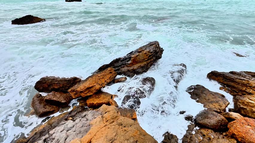The stunning rocky coastline features turquoise waves crashing against stones, perfect for capturing nature photos