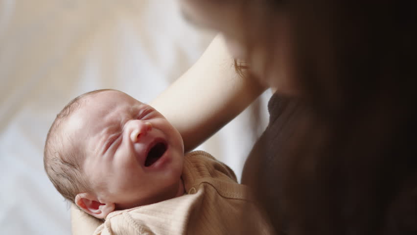 A peaceful newborn baby is held gently, sleeping soundly with closed eyes. A tender moment of early motherhood, captured in soft lighting.