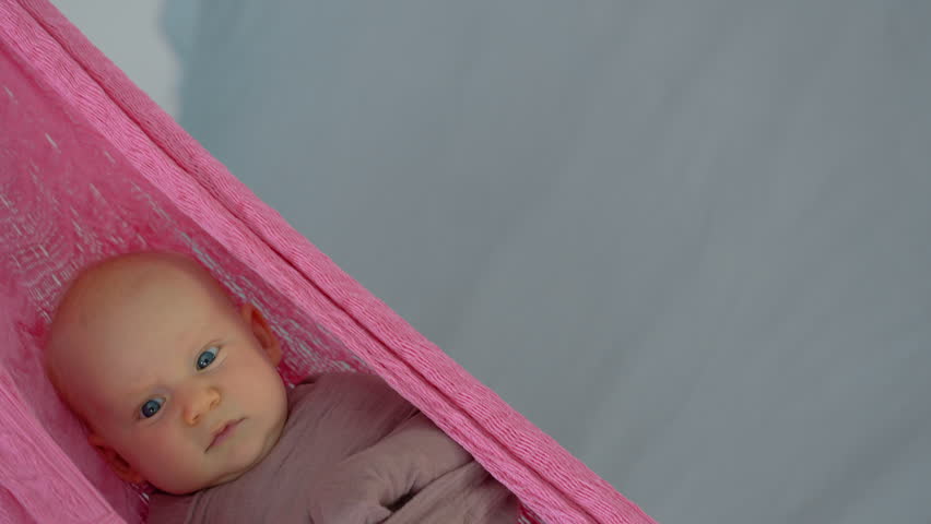 Loving mother gently swings her swaddled two-month-old baby in a hammock to help him fall asleep, creating a peaceful and nurturing family bedtime moment. Slowmotion video.