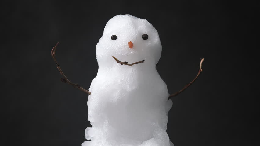 A small snowman melts gradually in this horizontal real-world video. Classic snow texture and iconic features on black background.