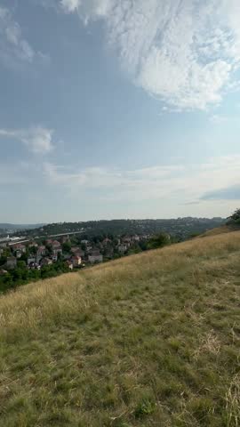 Hilltop landscape offers a panoramic view of a lively city, surrounded by greenery and under a bright blue sky with soft clouds, creating a peaceful environment