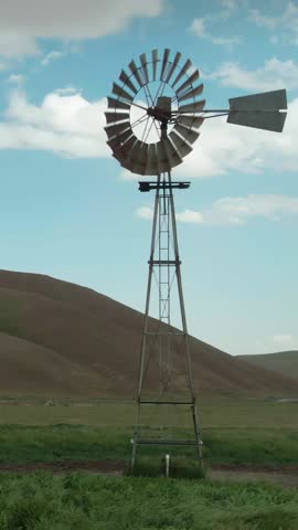 A weathered windmill stands tall in a rural landscape in Carrizo Plain National Monument, California, USA. The windmill is used to pump water for irrigation and livestock on the farm.