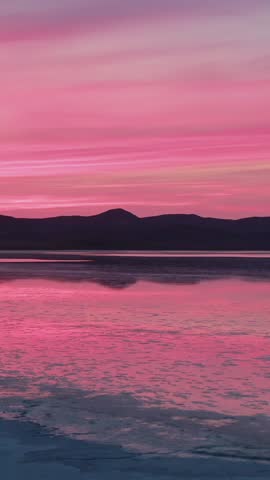 Pink sunset over sada lake in Carrizo Plain National Monument, California, USA. The mountains are silhouetted against the colorful sky, reflecting in the water. A serene landscape.