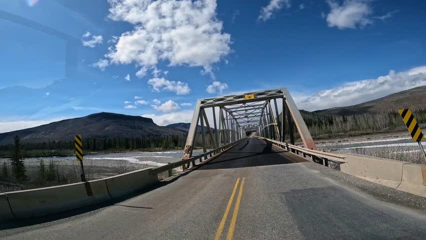 POV - driving over Racing River Bridge on the Alaska Highway in Northern Rocky Mountains in British Columbia; concepts of road less traveled and adventure travels