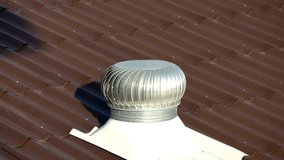 A rooftop ventilation system is spinning, promoting airflow above a brown metal roof under clear blue skies during daytime. The sunlight reflects off the metal surface. - Powered by Shutterstock - Get 15% off with code: PIKWIZARD15
