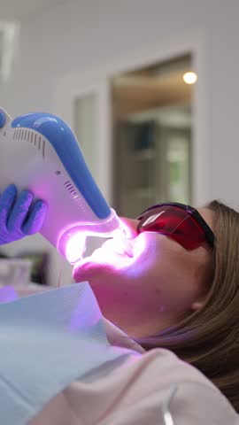 Patient undergoing dental whitening procedure with LED light for effective results. Vertical video
